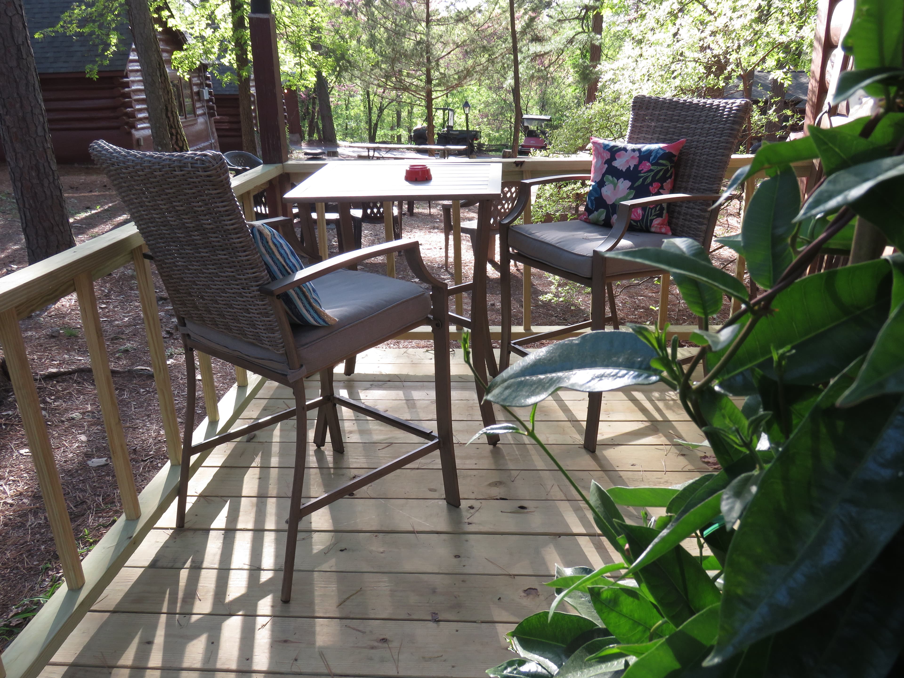 A cozy outdoor seating area on a wooden deck. The deck features a small square table with two high-backed wicker chairs.