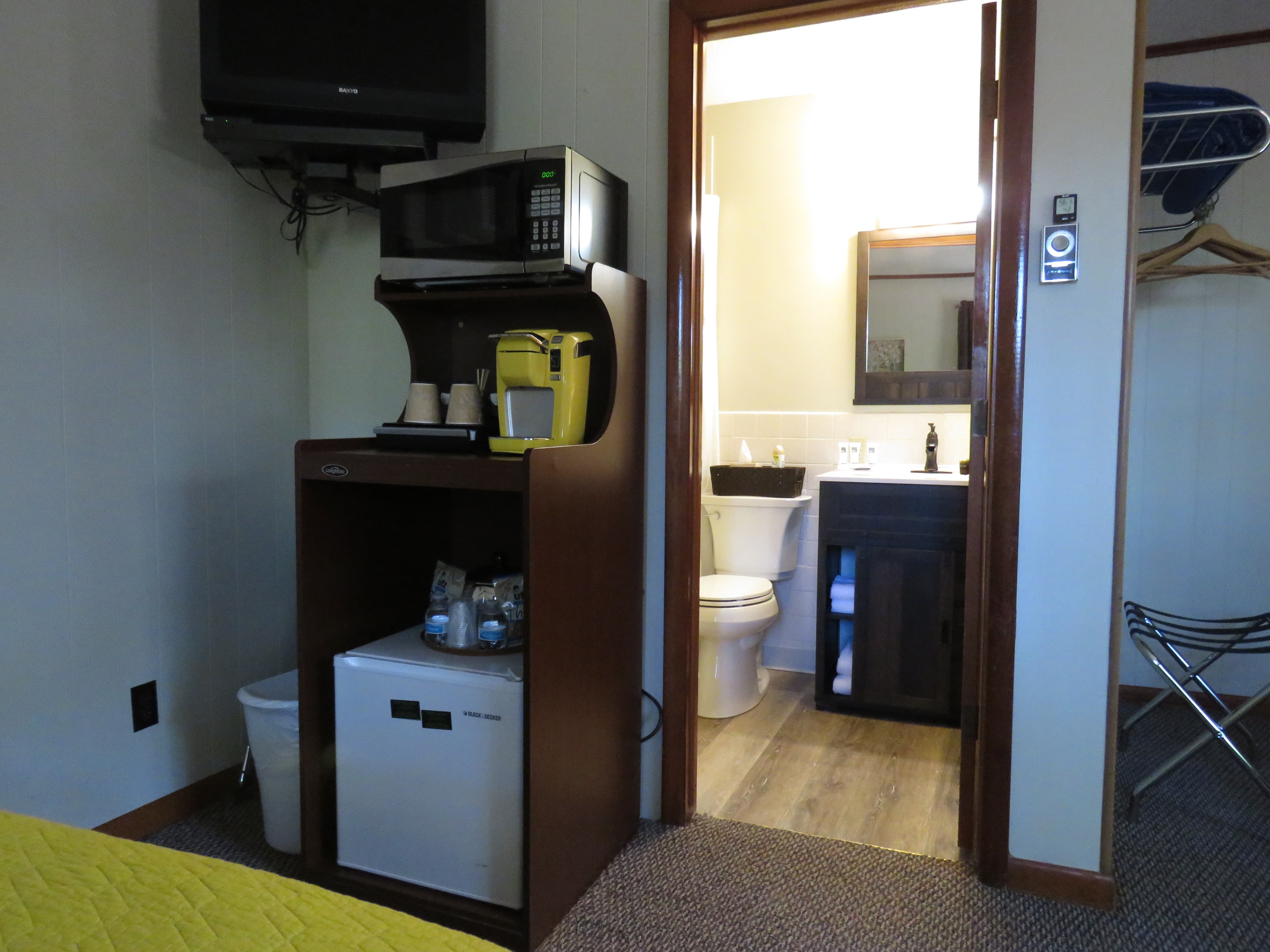 A bedroom with a microwave, coffee maker, and mini-fridge. The doorway on the right leads to a small bathroom.