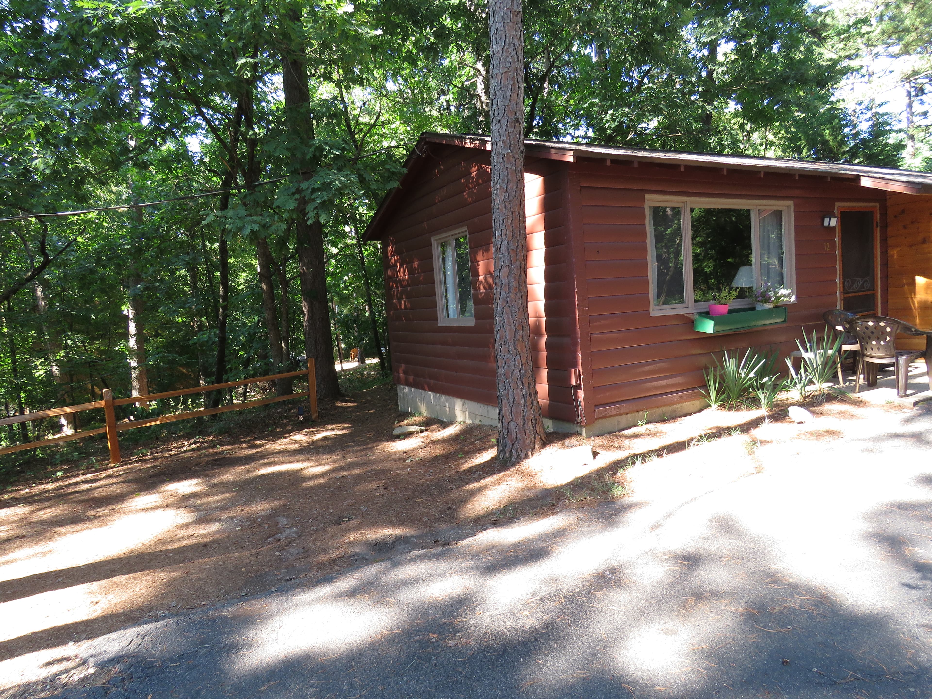 A charming, rustic cabin with a front window that has a flower box and a small porch. The cabin is surrounded by a natural wooded area.