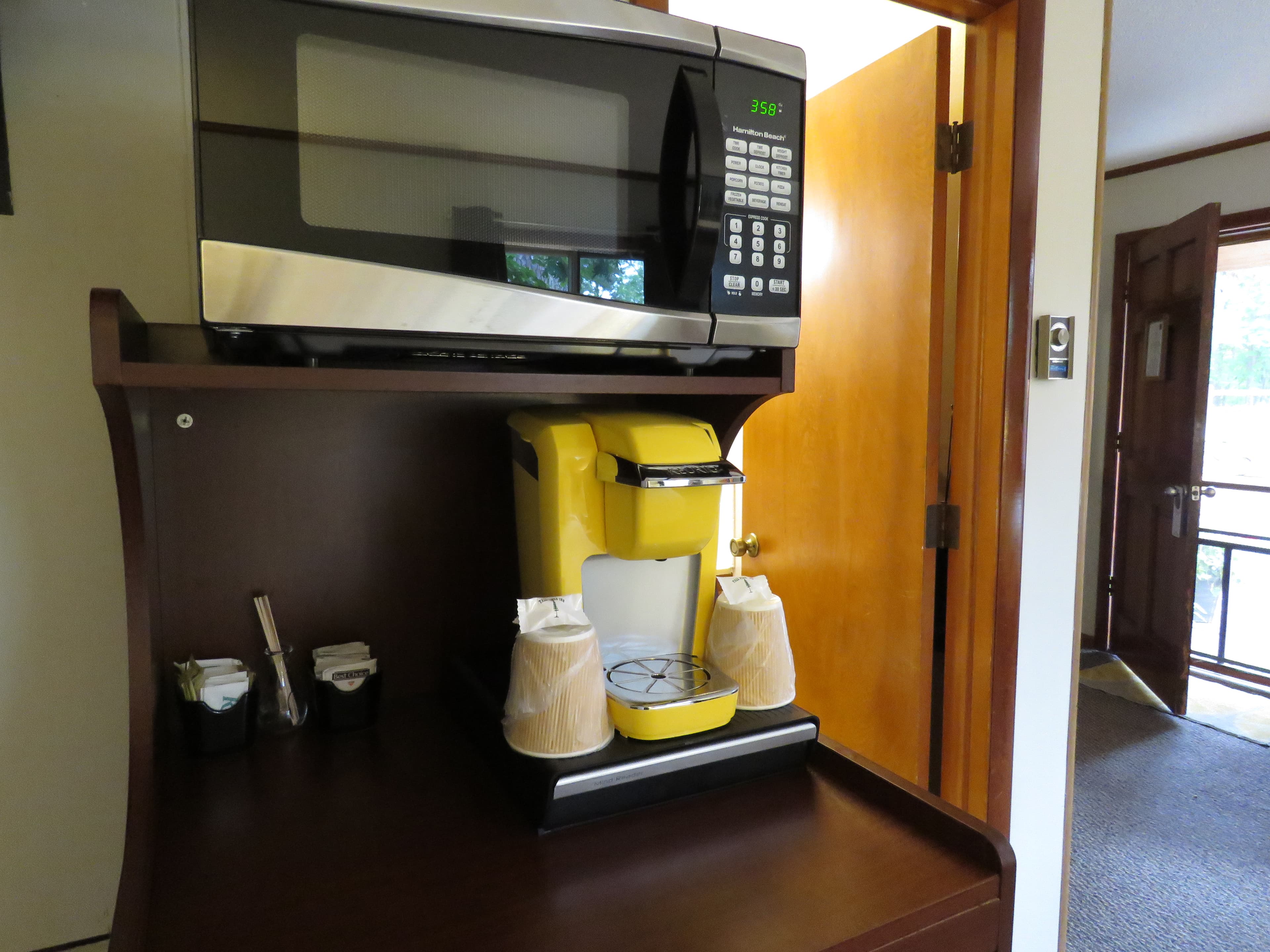 A close-up of a beverage center with a coffee maker, a microwave, and paper cups.