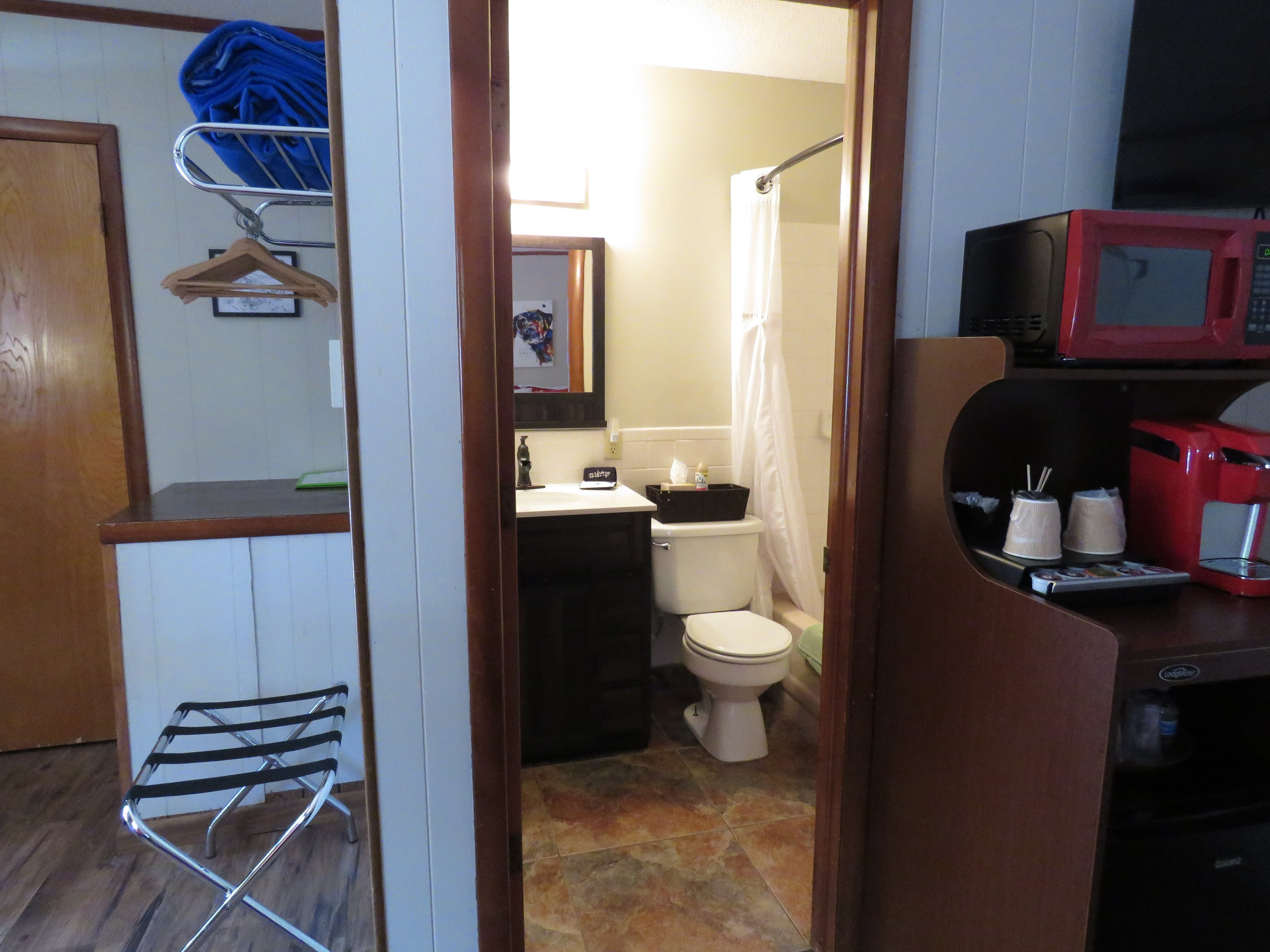 A view from inside the bedroom looking towards a compact bathroom. The doorway reveals a toilet, a sink, and a shower with a white curtain.