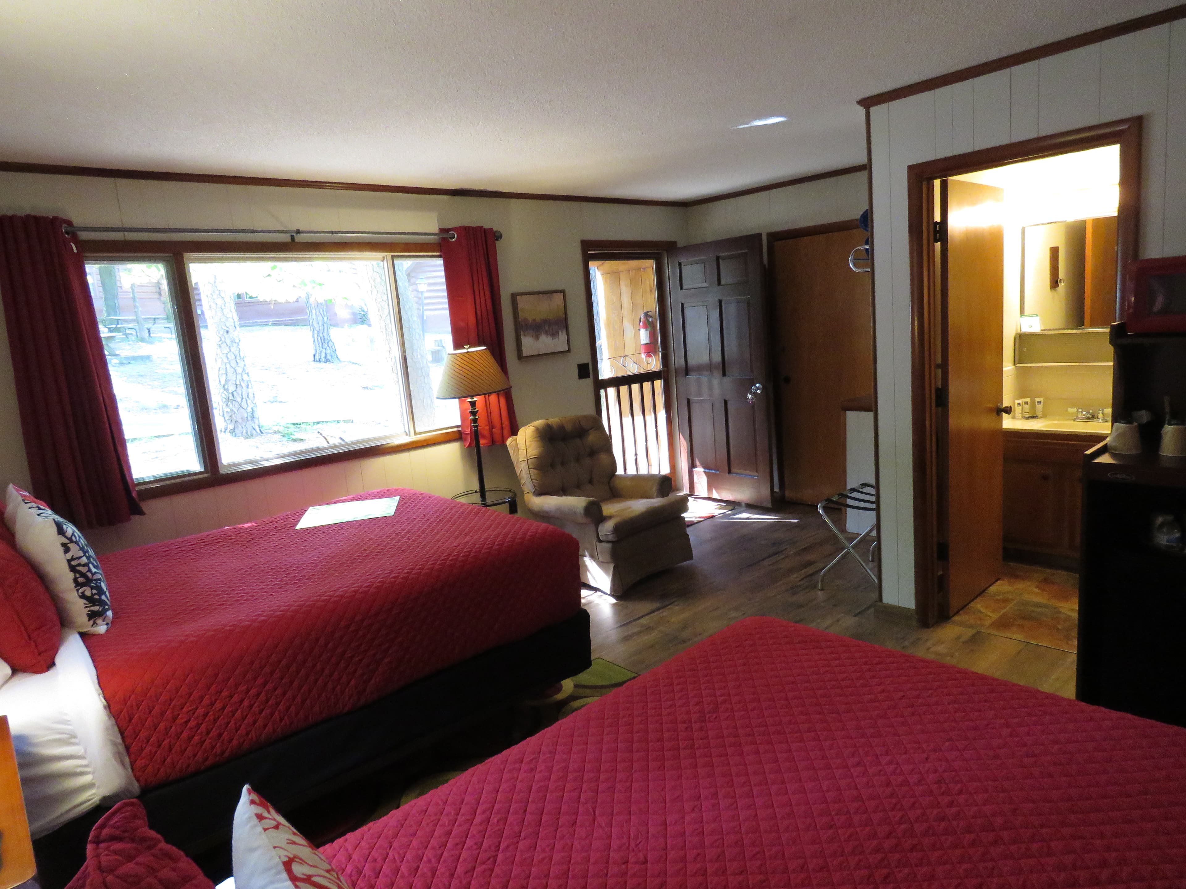 A bedroom features two beds with bright red quilts and dog-themed art on the walls. A colorful, patterned rug is on the floor.