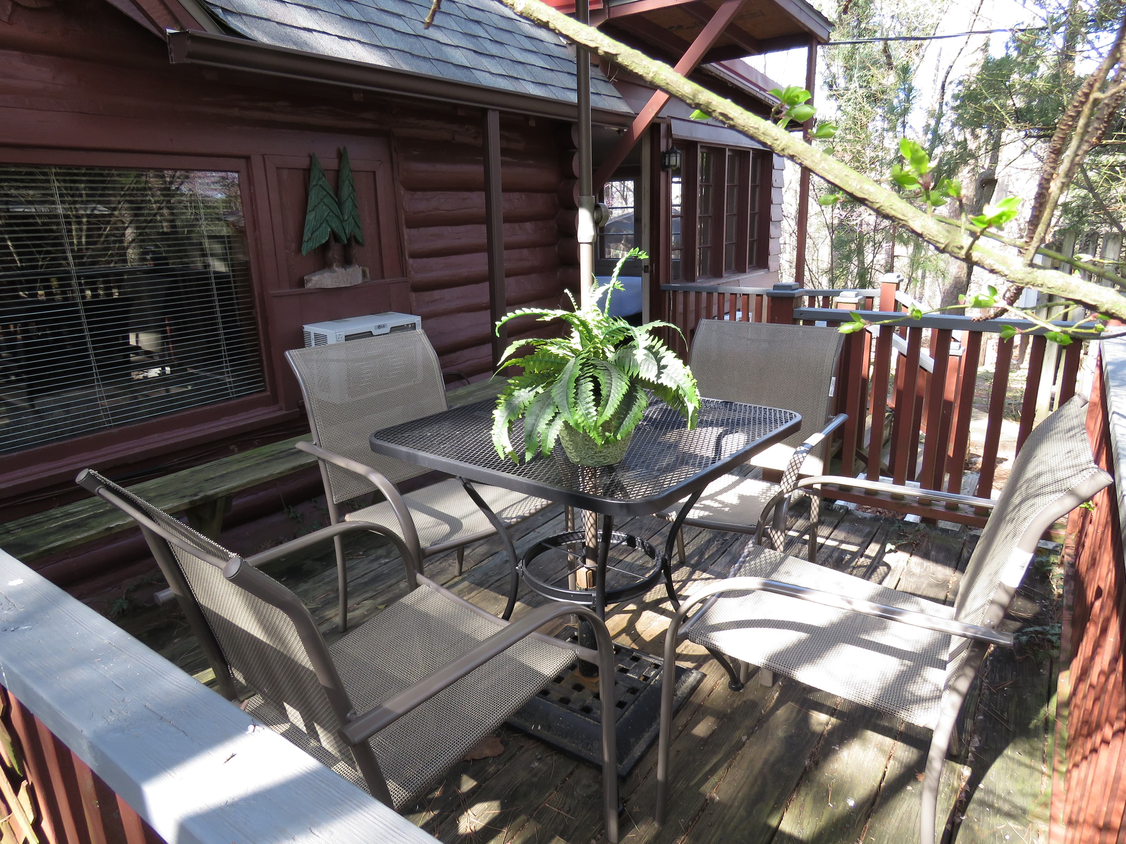 A cozy outdoor dining area on a wooden deck with a square metal table, four chairs, and a small plant.