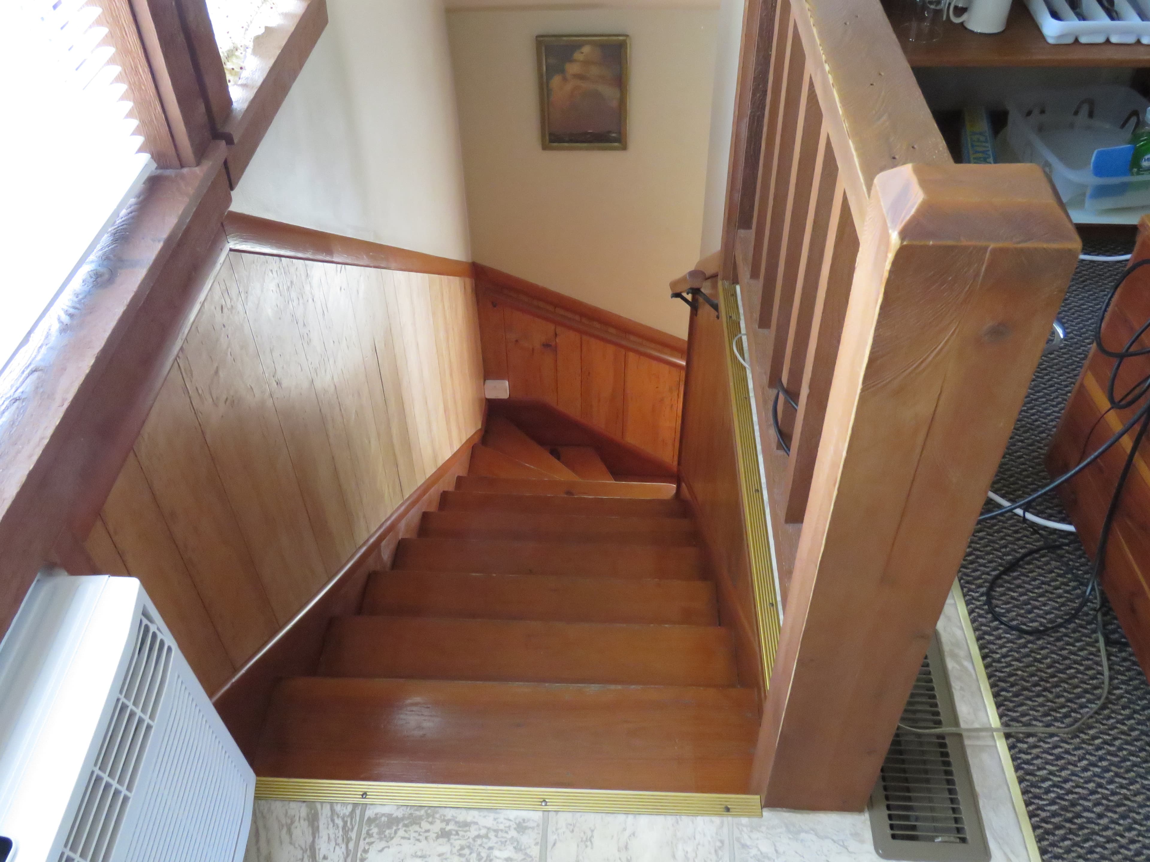 A staircase with wood steps, wood banisters, and wainscoting. A small framed picture hangs on the wall, and there is a heater on the left.