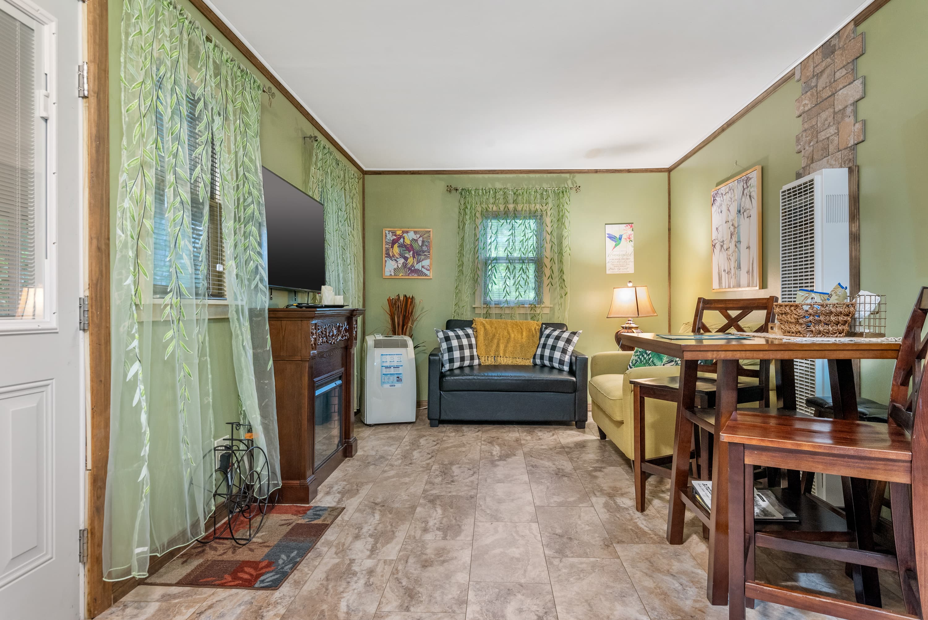 A living room and dining area with light green walls. The space features a small dining table, a couch, a loveseat, and a TV stand.