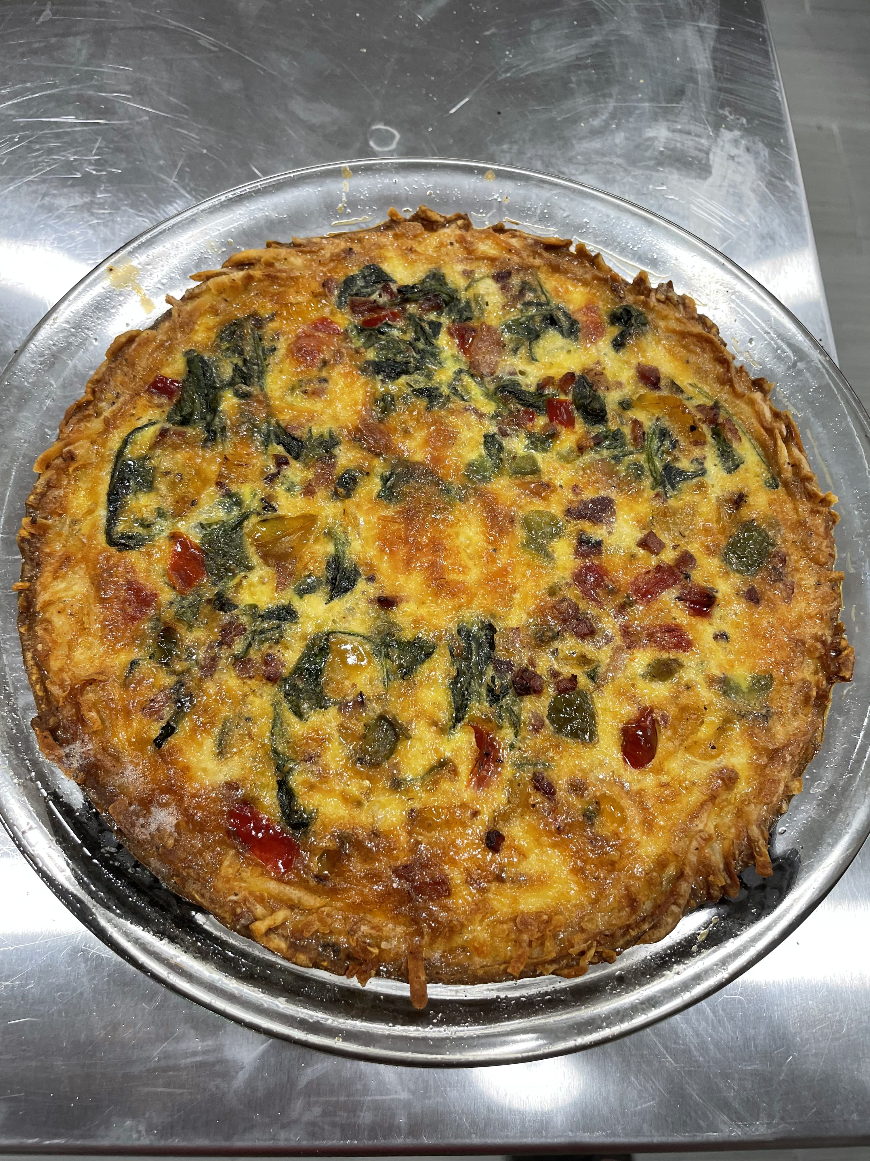 A golden-brown quiche filled with spinach, peppers, and cheese in a glass pie dish.