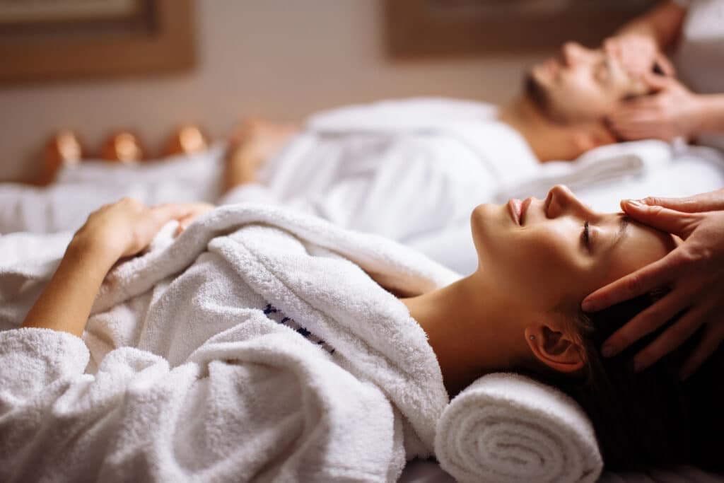 A woman relaxes during a spa treatment while a man receives a massage in the background.