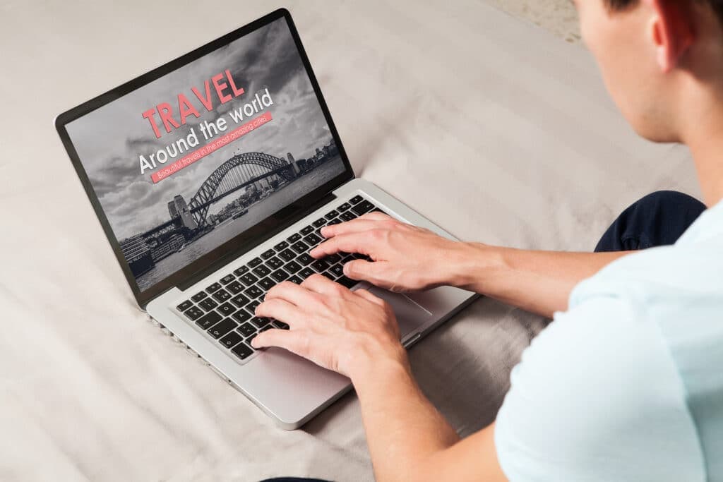 A person typing on a laptop displaying a travel-themed website with a Sydney harbor image.