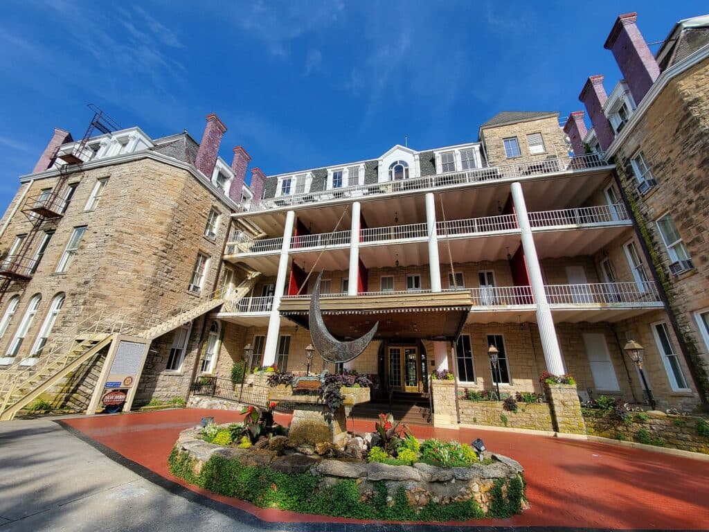 Historic stone hotel with multiple balconies and a landscaped entrance.