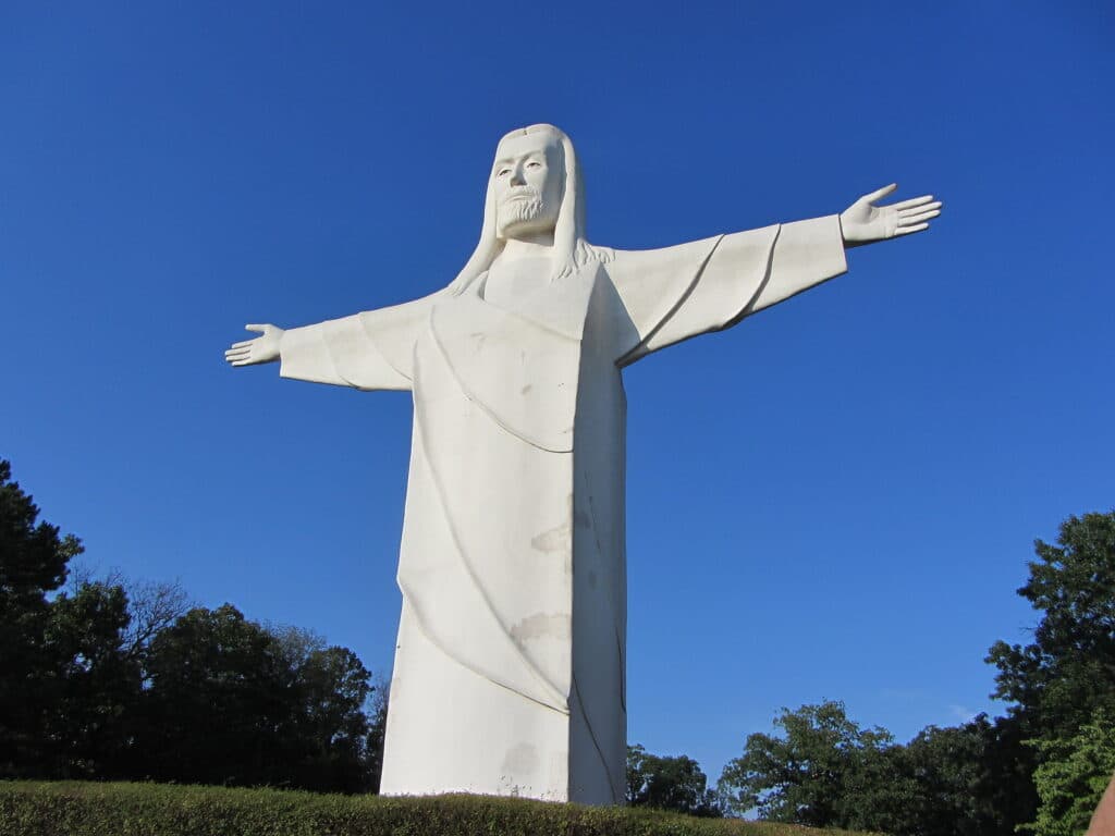 A towering white statue of Jesus Christ with outstretched arms against a clear blue sky.