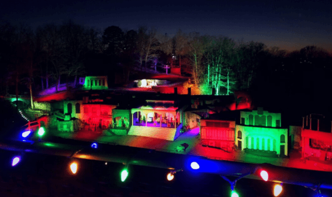 A brightly lit miniature town is illuminated with colorful lights at dusk.
