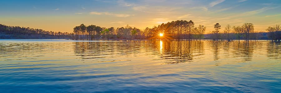 Sunrise over a calm lake with silhouetted trees on the horizon.