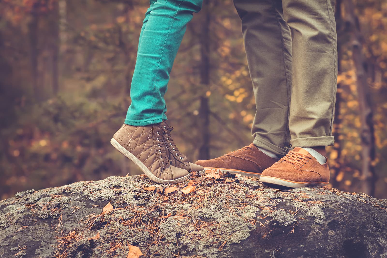 A couple stands on a rock, their feet close together amid autumn foliage.