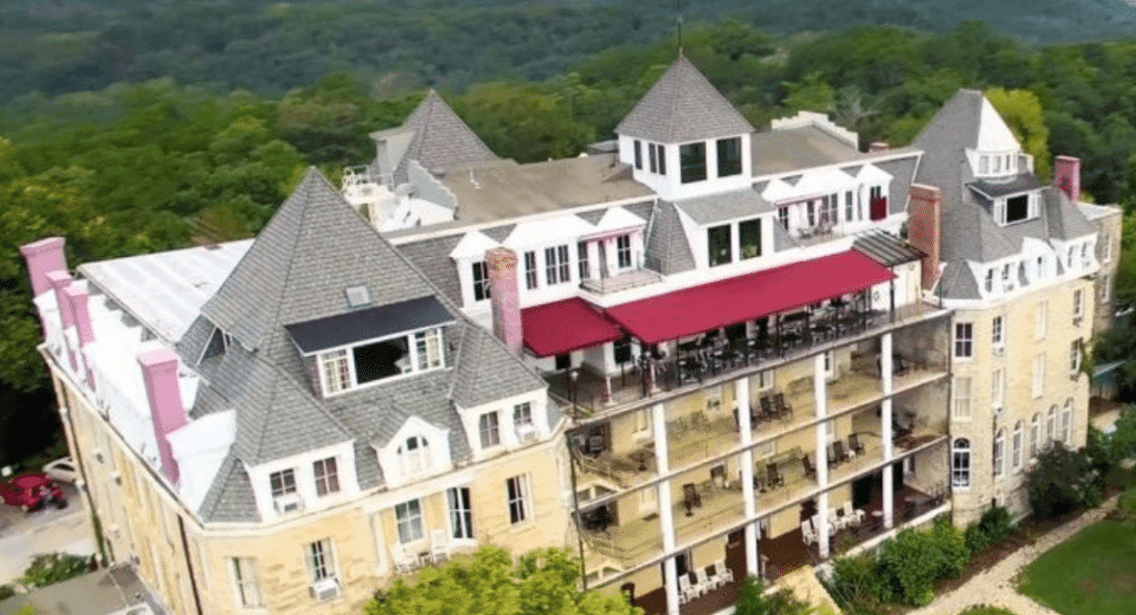 Aerial view of a large, ornate building with peaked roofs surrounded by greenery.
