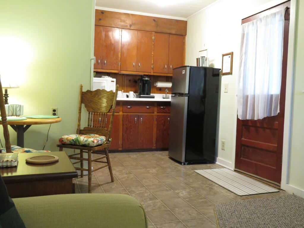 A small kitchen area with wooden cabinets, a black refrigerator, and a cheerful chair beside a table.
