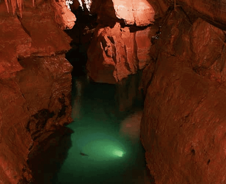 A subterranean river flows through a deep, reddish canyon illuminated by soft lighting. A subterranean river flows through a deep, reddish canyon illuminated by soft lighting.