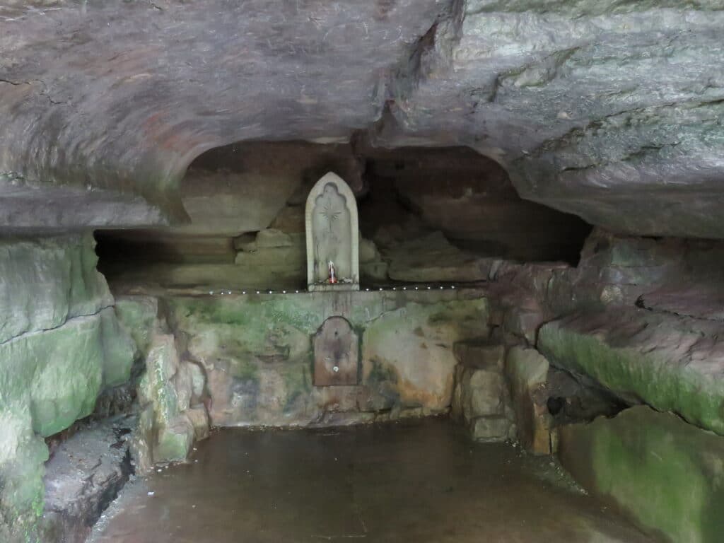 A small, dimly lit cave interior featuring a stone statue on a ledge.