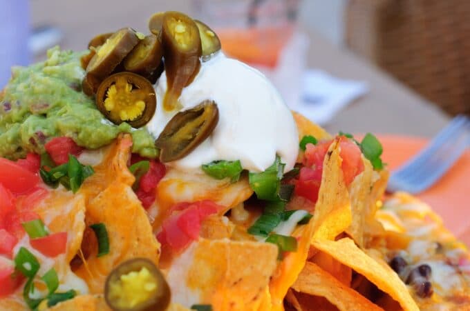 A close-up of nachos topped with jalapeños, guacamole, sour cream, diced tomatoes, and green onions.