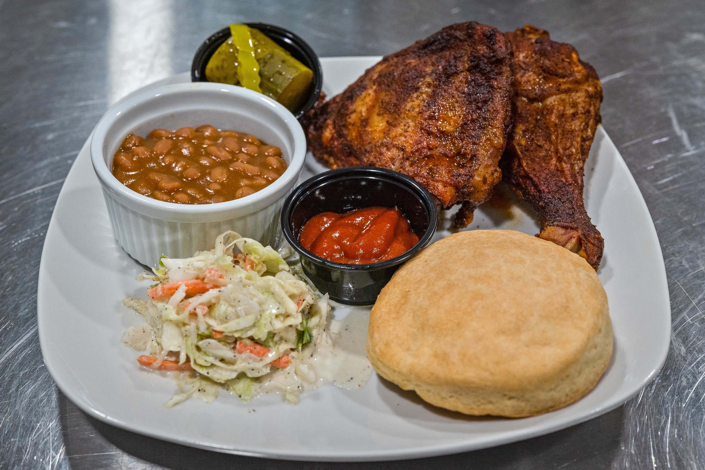 A plate featuring fried chicken, baked beans, coleslaw, a biscuit, and pickles.