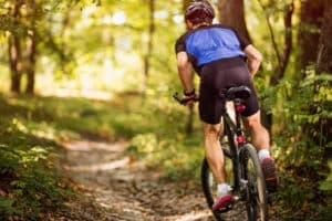 A cyclist rides on a forest trail surrounded by greenery.