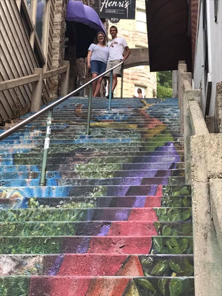 A couple stands on colorful, painted stairs with greenery and vibrant patterns.