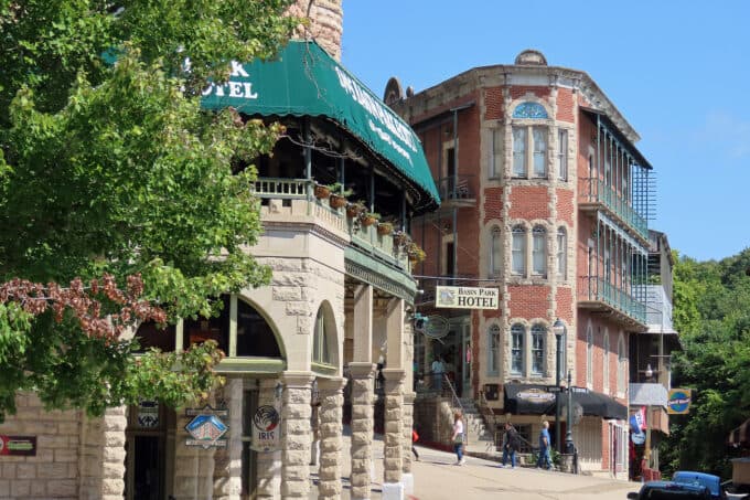 Historic buildings line a sunny street, featuring the "Basin Park Hotel" and vibrant storefronts.