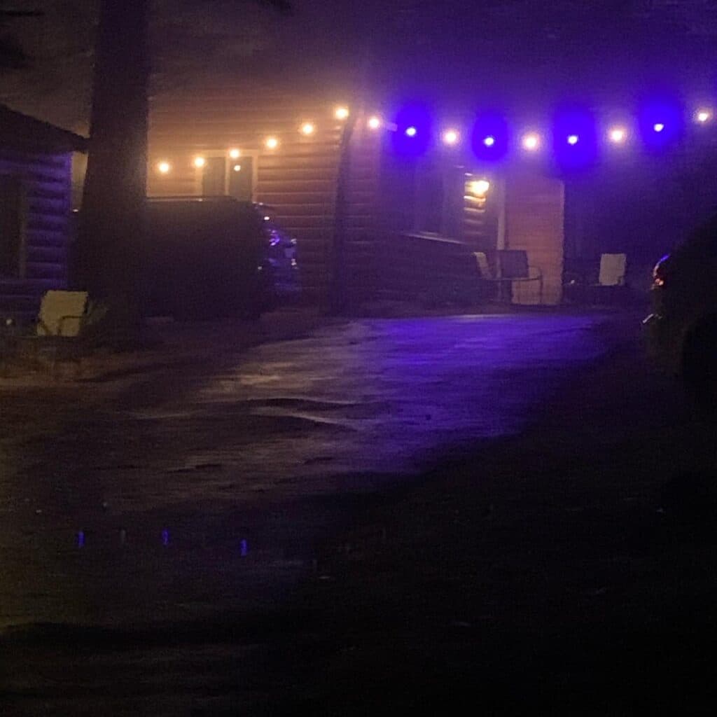 A dimly lit cabin surrounded by fog, featuring string lights and a gravel driveway.