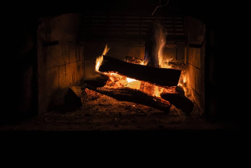 A flickering fire burns in a stone fireplace against a dark background.