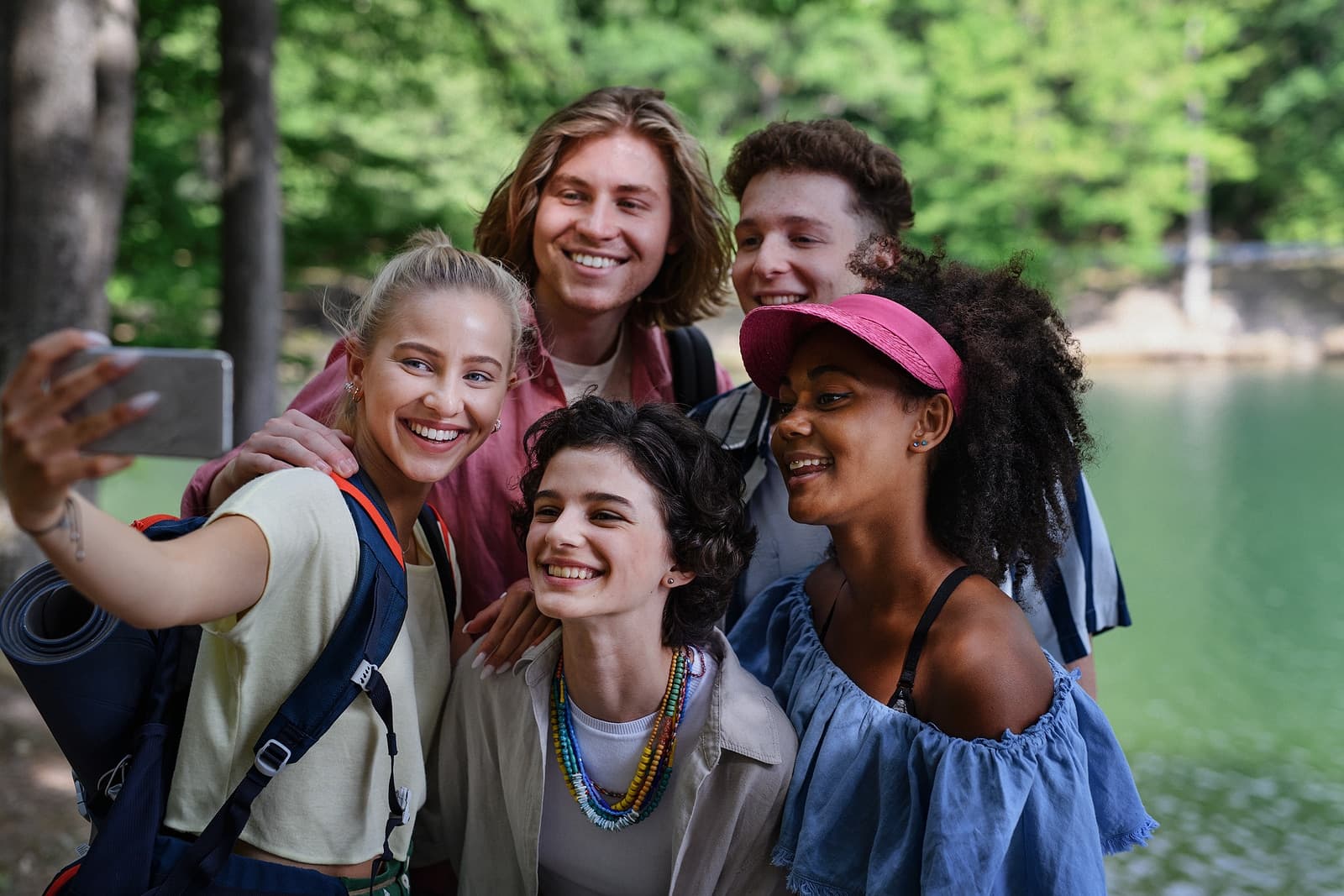 A group of five friends poses for a cheerful selfie near a serene lake.