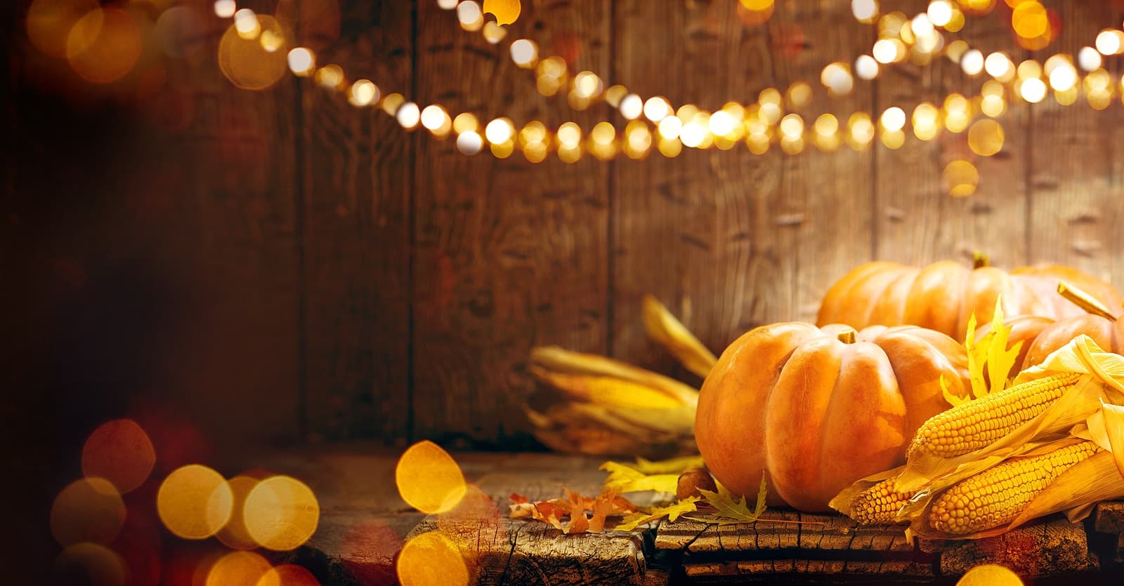 A cozy autumn scene featuring pumpkins, corn, and warm lighting against a wooden backdrop.