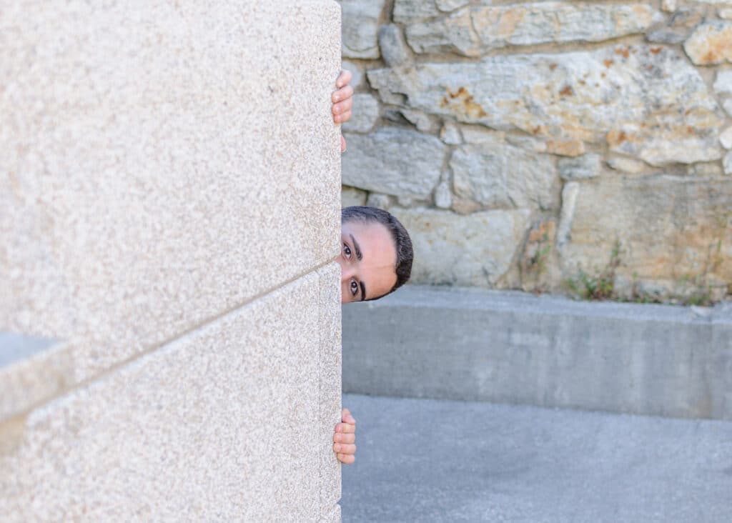 A person peeks around a stone structure with a playful expression.