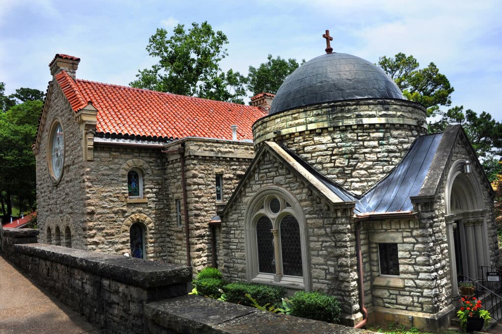 A stone church with a dome and red tile roof nestled among trees.