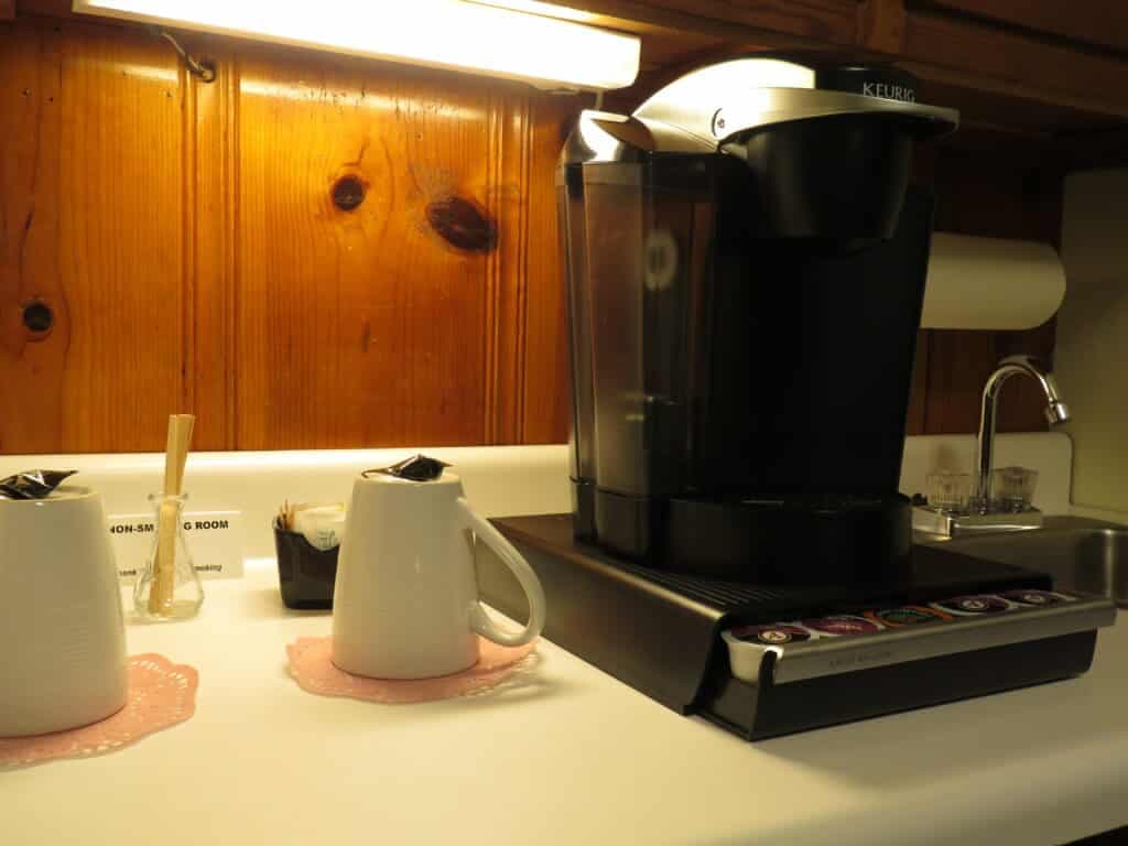 A Keurig coffee maker sits on a countertop next to two white mugs and a creamer container.