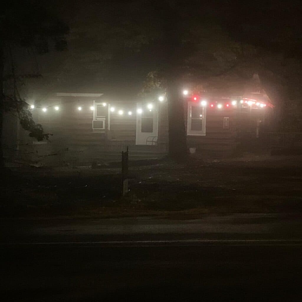 A dimly lit house in the fog adorned with string lights.
