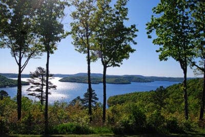 Scenic view of a sparkling lake surrounded by green hills and trees under a clear blue sky.