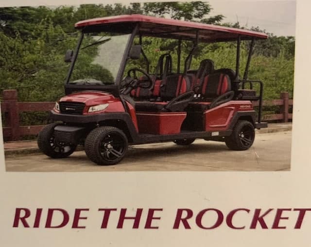 A red and black golf cart parked on a path surrounded by greenery.