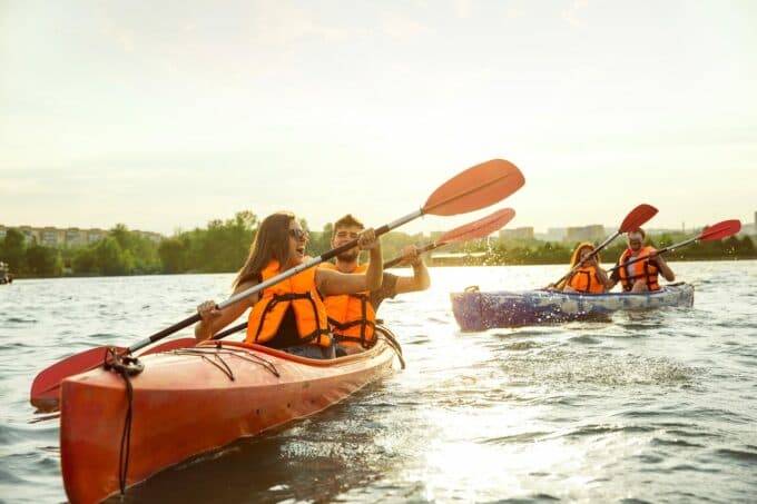 Two kayaks with four people enjoying a sunny day on the water, wearing life jackets and paddling.