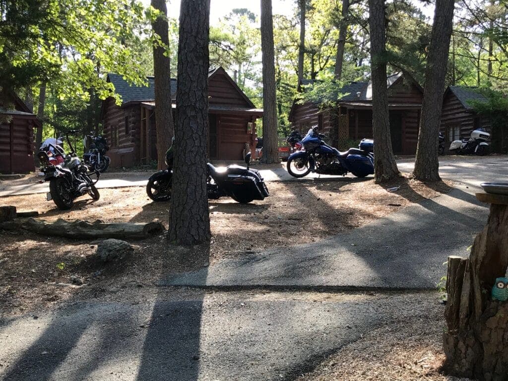 Motorcycles parked near cabin-style lodges in a wooded area.