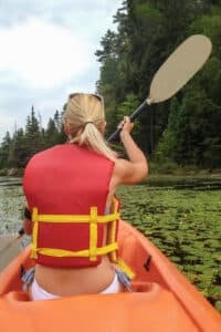 A person paddles a kayak in a green, serene outdoor setting.