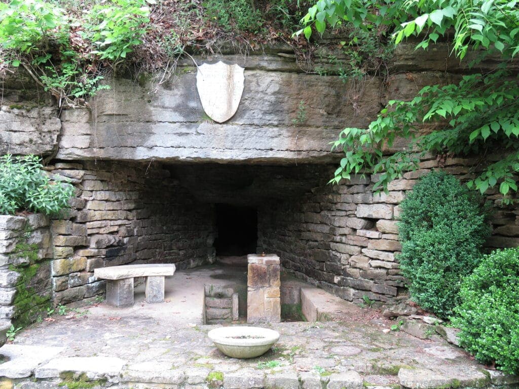 An arched stone entrance with a shield emblem surrounded by greenery, leading into a dark cavern.