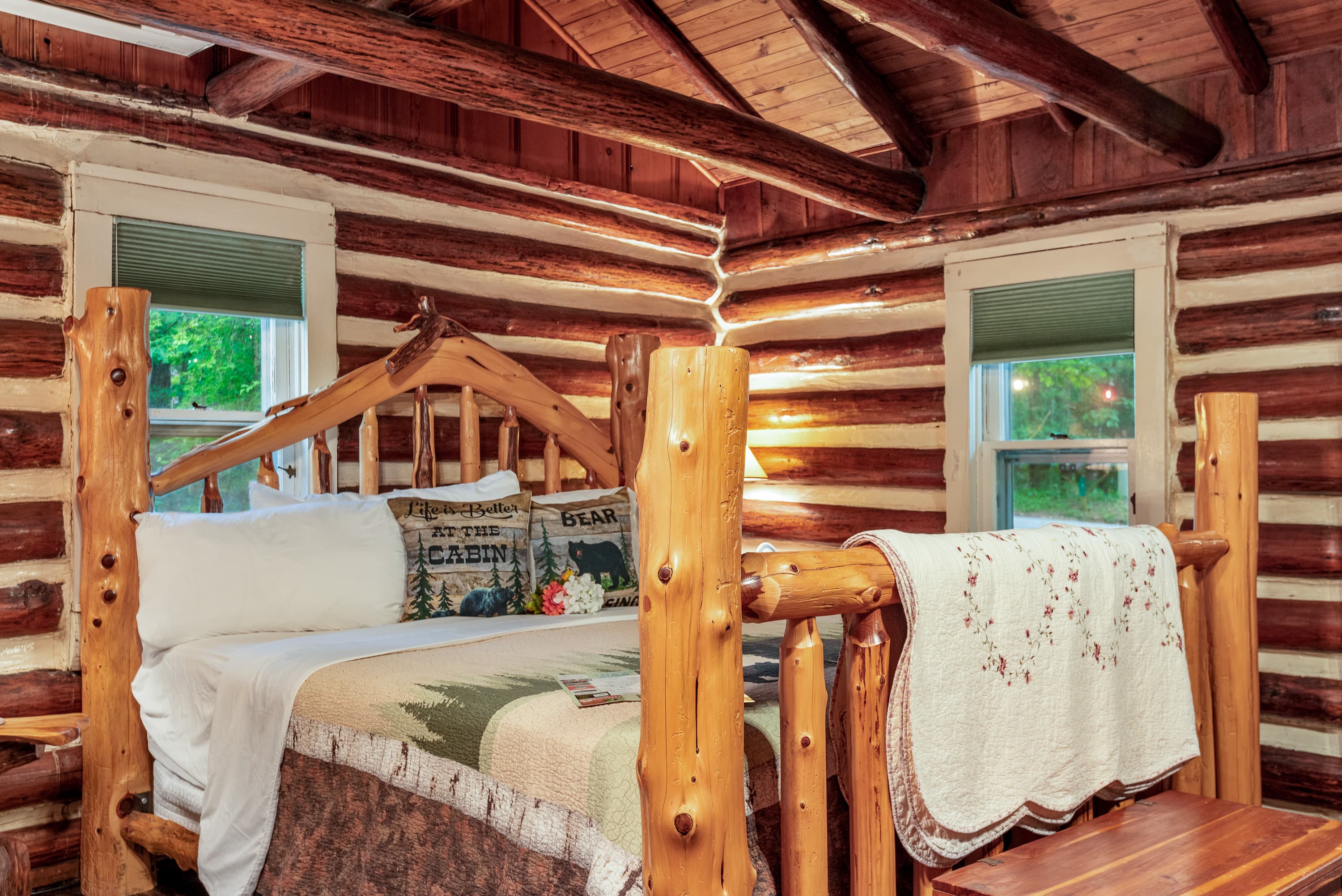Cozy log cabin bedroom featuring a wooden bed, quilts, and rustic decor.
