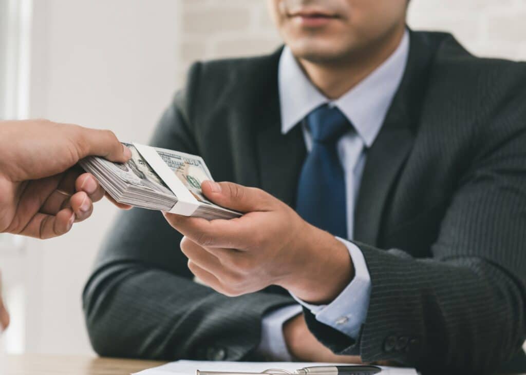 A person hands a bundle of money to another individual in a business setting.