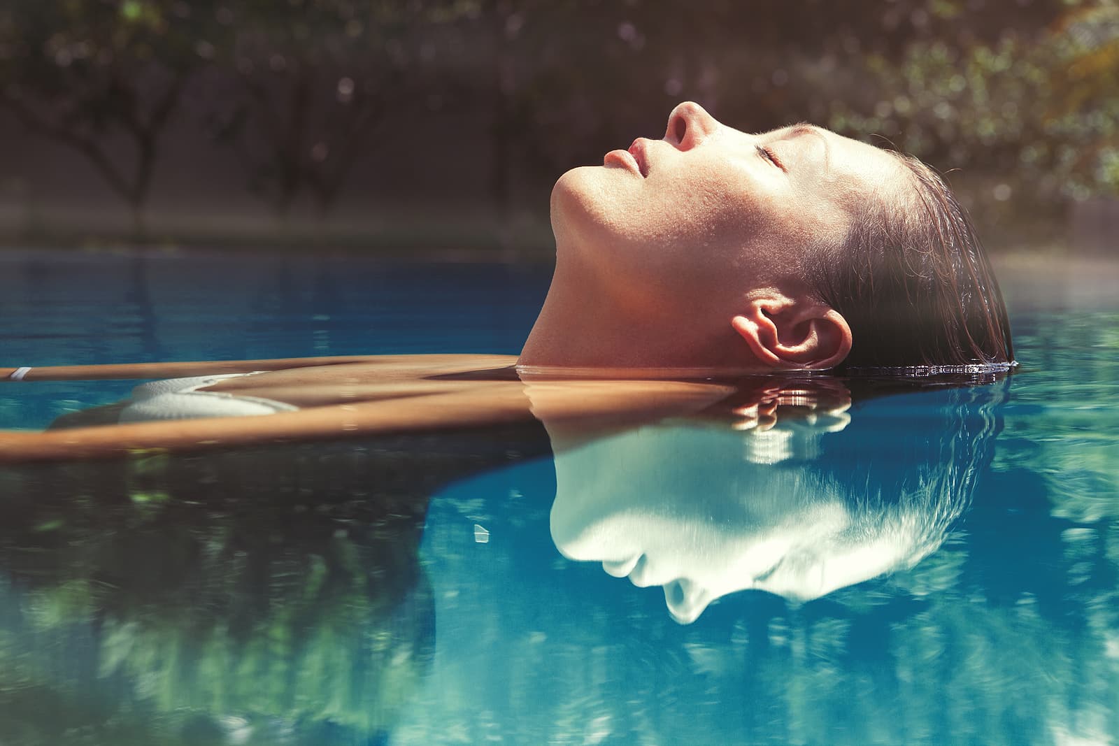A woman floats serene on her back in a pool, with gentle sunlight reflecting on the water.