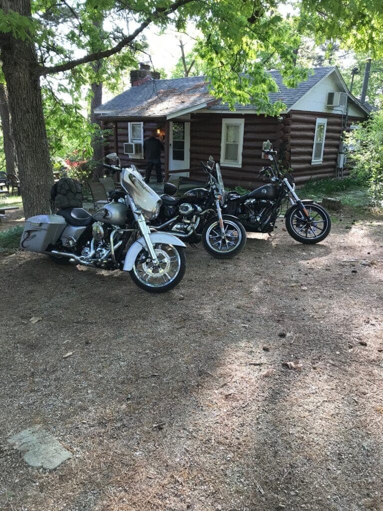Three motorcycles parked in front of a log cabin surrounded by trees.