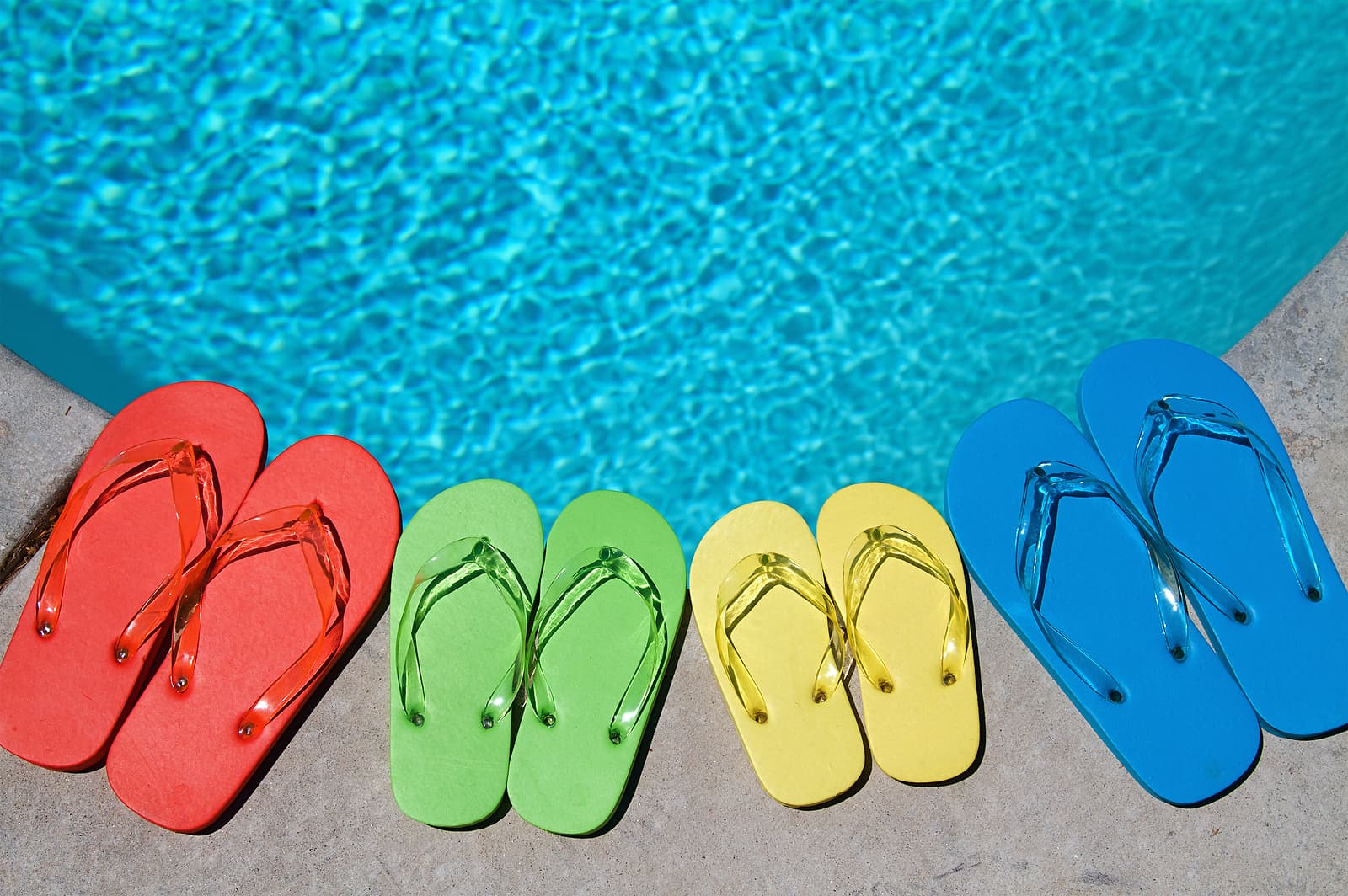 A row of colorful flip-flops sits by a sparkling blue pool. A row of colorful flip-flops sits by a sparkling blue pool.