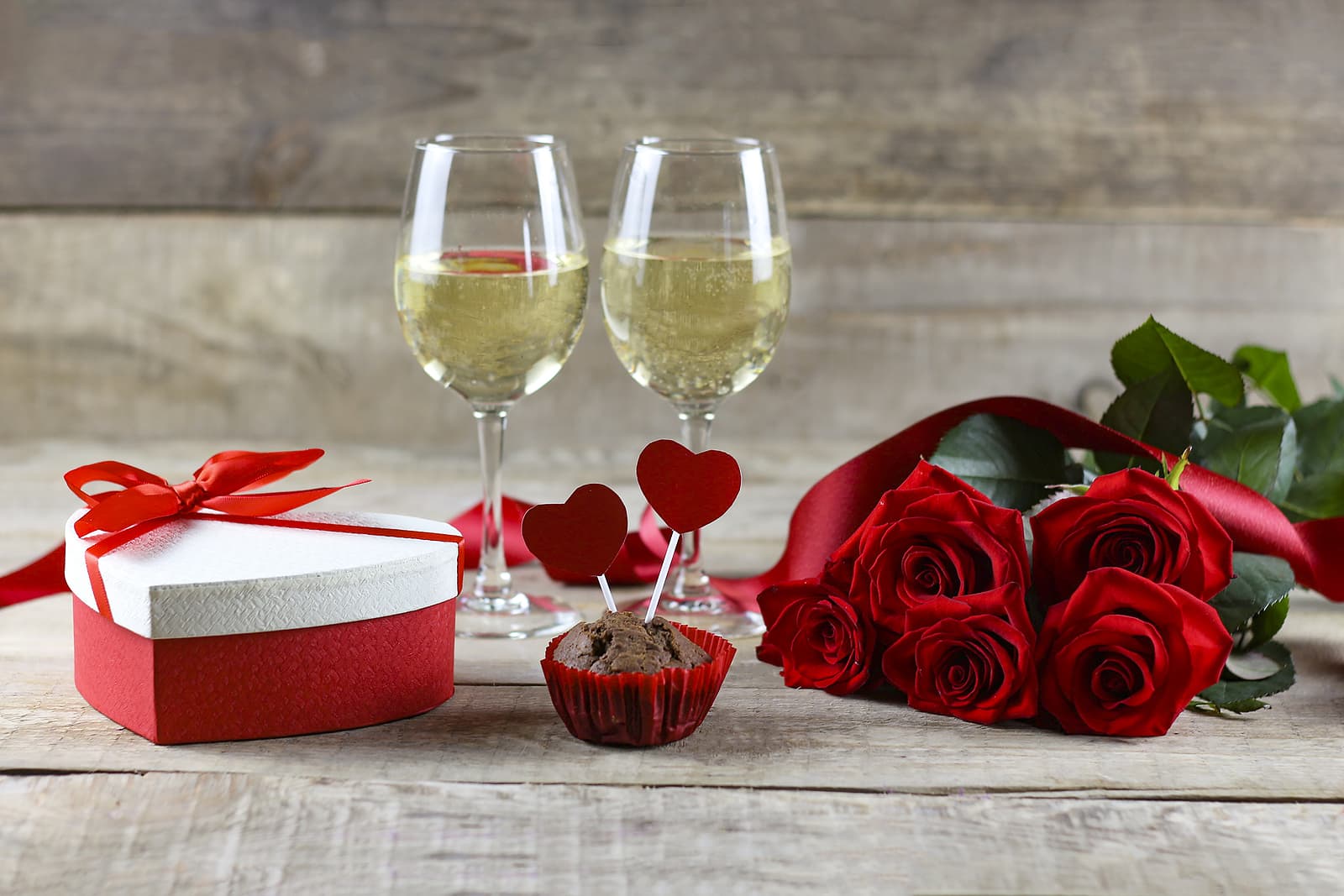Two glasses of white wine sitting by a heart box of candy and a bouquet of roses Two glasses of white wine sitting by a heart box of candy and a bouquet of roses