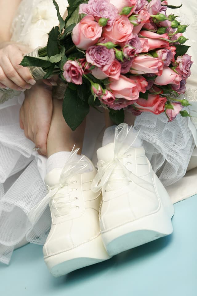 bride in white dress sitting on floor wearing white tennis shoes