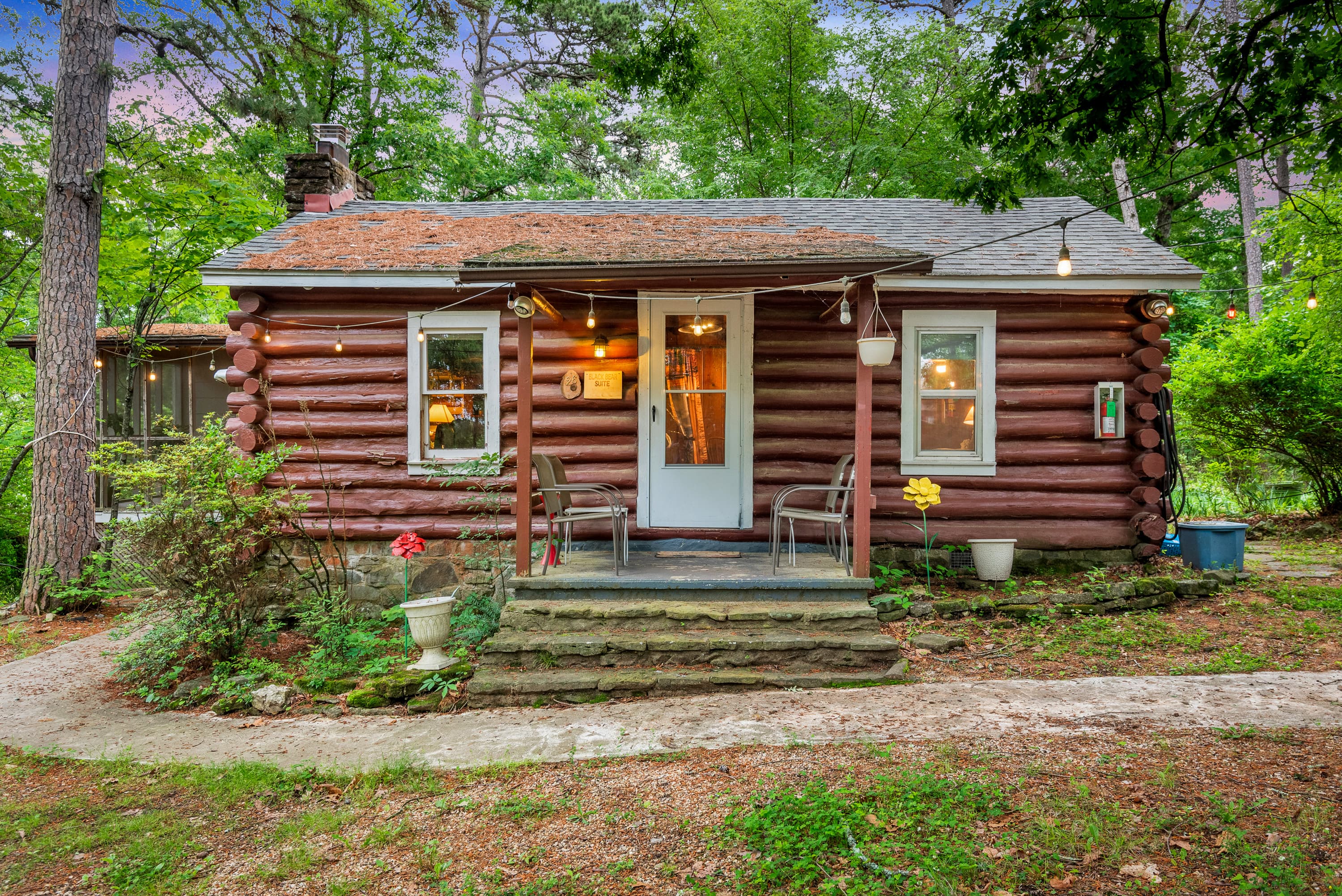 Historic log cabin with porch and four chairs a walkway and greenery line the front Historic log cabin with porch and four chairs a walkway and greenery line the front