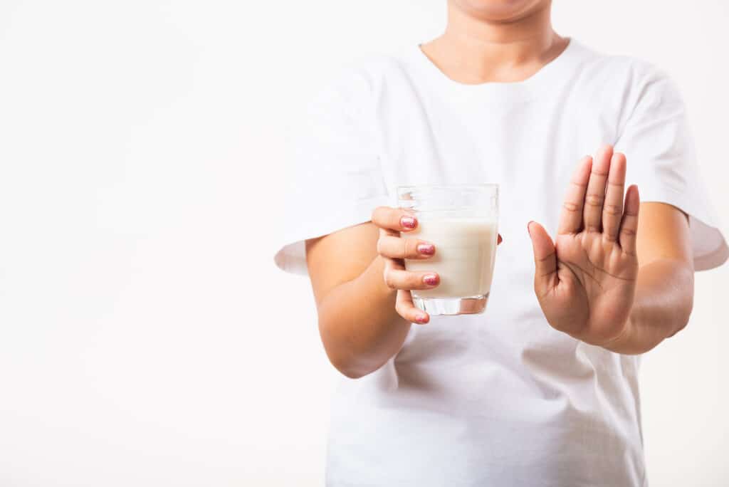 woman raising her hand to say no to a glass of milk