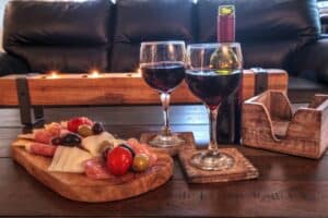 wood board with various cheese and meat snacks and two glasses of red wine next to it